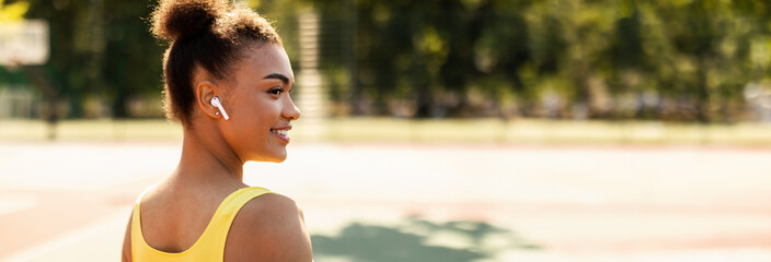 Portrait of half-turned smiling African American lady wearing wireless headphones, exercising...