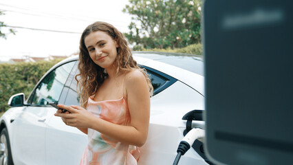 Young woman use smartphone to pay for electricity at public EV car charging station in nature....
