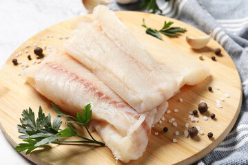 Pieces of raw cod fish, spices and parsley on table, closeup