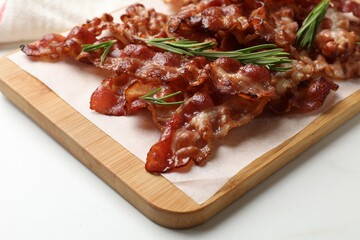 Slices of tasty fried bacon with rosemary on white table, closeup