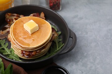 Tasty pancakes with butter, fried bacon and fresh arugula on grey table. Space for text
