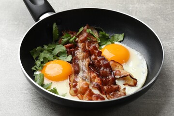 Tasty bacon, eggs and parsley in frying pan on gray textured table, closeup
