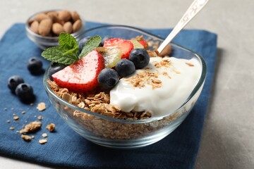 Tasty granola with berries, yogurt and mint on grey table