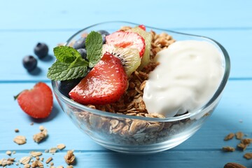 Tasty granola with berries, yogurt and mint on light blue wooden table, closeup
