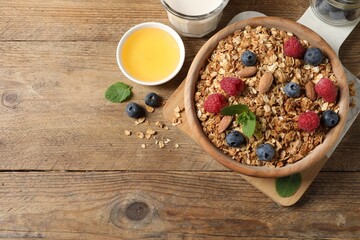 Tasty granola with berries, nuts and mint on wooden table, flat lay