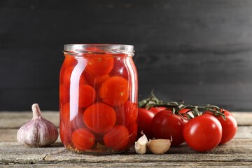 Tasty pickled tomatoes in jar, fresh vegetables and garlic on wooden table