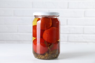 Tasty pickled tomatoes in jar on white table