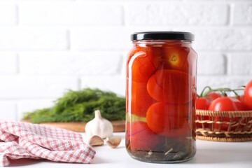 Tasty pickled tomatoes in jar and garlic on white table