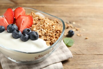 Tasty granola with berries and yogurt in bowl on wooden table, closeup. Space for text