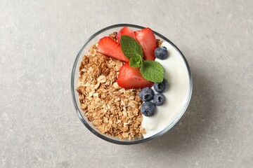 Tasty granola with berries and yogurt in bowl on grey textured table, top view