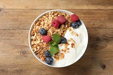 Tasty granola with berries and yogurt on wooden table, top view