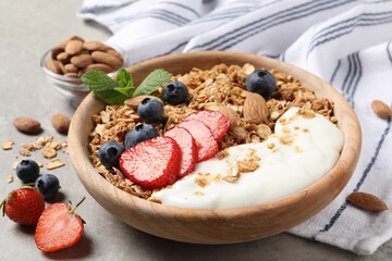 Tasty granola with berries, almond and yogurt in bowl on grey textured table, closeup