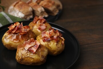 Delicious baked potatoes with bacon on wooden table, closeup. Space for text