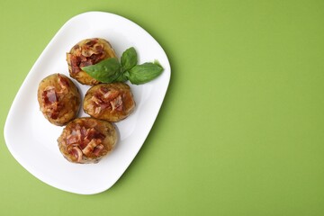 Delicious baked potatoes with bacon and basil on green background, top view. Space for text