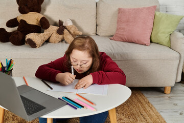 A little girl with Down syndrome draws on a notebook at home.
