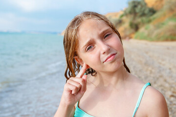 The child got water in his ear while swimming in the sea. The girl cleans her ear from water.