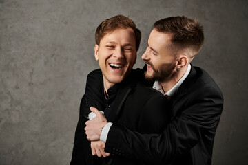Two men in suits embrace and laugh together.