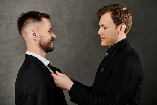 Two men in elegant suits stand close, one adjusting the others tie.