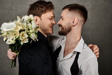 Two men in elegant suits share a loving moment, one holding a bouquet of white flowers.