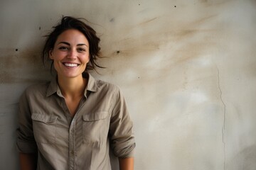 Portrait of a grinning woman in her 30s sporting a breathable hiking shirt in bare concrete or plaster wall