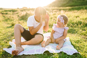 Fototapeta premium Kids playing in mountains on summer day. Happy children hug and sit on blanket in green grass in field at sunset. Older brother plays with younger sister in spring sunlight. Spending time together.