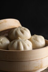Delicious bao buns (baozi) in bamboo steamer on table against black background, closeup