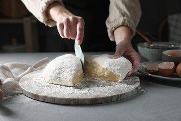 Woman cutting dough at grey table, closeup
