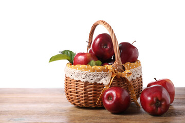 Fresh ripe red apples in wicker basket on wooden table against white background