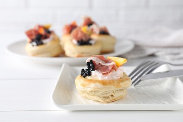 Delicious puff pastry with cream cheese, ham, black caviar, peach and cutlery on white wooden table, closeup