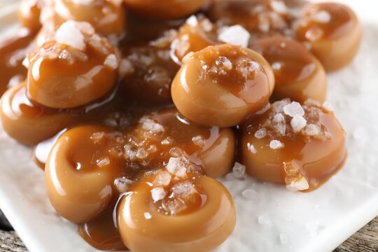 Tasty candies, caramel sauce and salt on wooden table, closeup