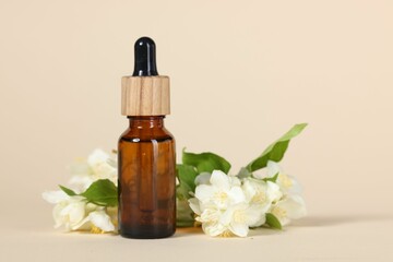 Essential oil in bottle and beautiful jasmine flowers on beige background, closeup