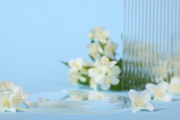 Presentation of product. Glass podium and beautiful jasmine flowers on light blue background, space for text