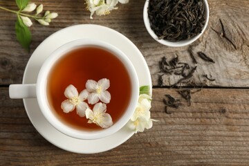 Aromatic jasmine tea in cup, flowers and dry leaves on wooden table, flat lay