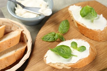 Delicious sandwiches with cream cheese and basil leaves on wooden table, closeup