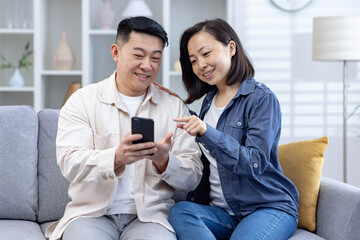 Happy couple sitting on a couch and using a smartphone together in a comfortable and cozy living room.