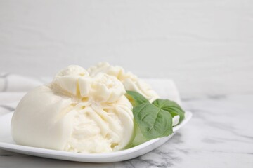 Delicious burrata cheese and basil on white marble table, closeup. Space for text