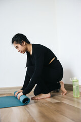 Young woman rolling her  yoga mat after a yoga class on wooden floor 
