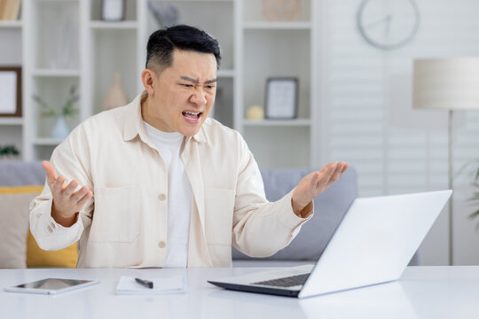 Man showing frustration and anger while looking at laptop in home office setting. Concept of technology issues, work stress, and negative emotions.
