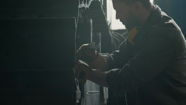 Heavy equipment mechanic in hardhat and gloves using wrench for repairing bulldozer at work in machine factory