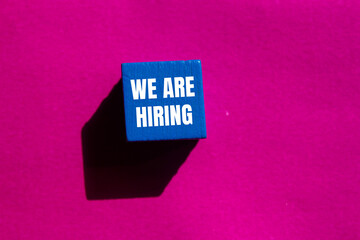 We are hiring message written on blue wooden cube with pink background. Conceptual we are hiring...