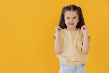 A little girl clenched her fists and shows anger on a yellow background