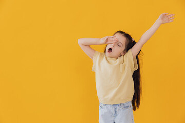 Sleepy little girl yawning on yellow studio background