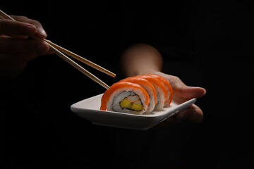 Hand holding plate of Uramaki sushi or California salmon roll on black background. Japanese food style concept