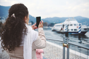 Woman taking photo of a boat on a scenic lake with mountains in the background