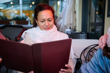 Woman reading menu at outdoor cafe wearing a white scarf