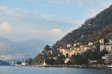 Scenic view of a lakeside village nestled among lush hills with serene waters and a cloudy sky