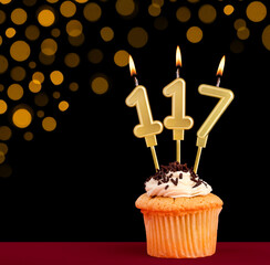 Birthday candle with cupcake - Number 117 on black background with out of focus lights