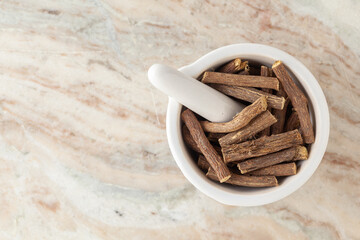 Top-view of Dry Organic Liquorice or Mulethi (Glycyrrhiza glabra), in white ceramic mortar and pestle, on a marble background.