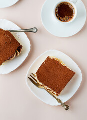 Two pieces of tiramisu and a cup of coffee, top view on a light background.