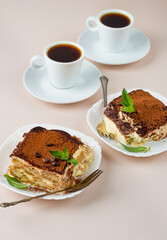 Two pieces of tiramisu with mint leaf, coffee beans and cups of espresso coffee. Classic Italian dessert.